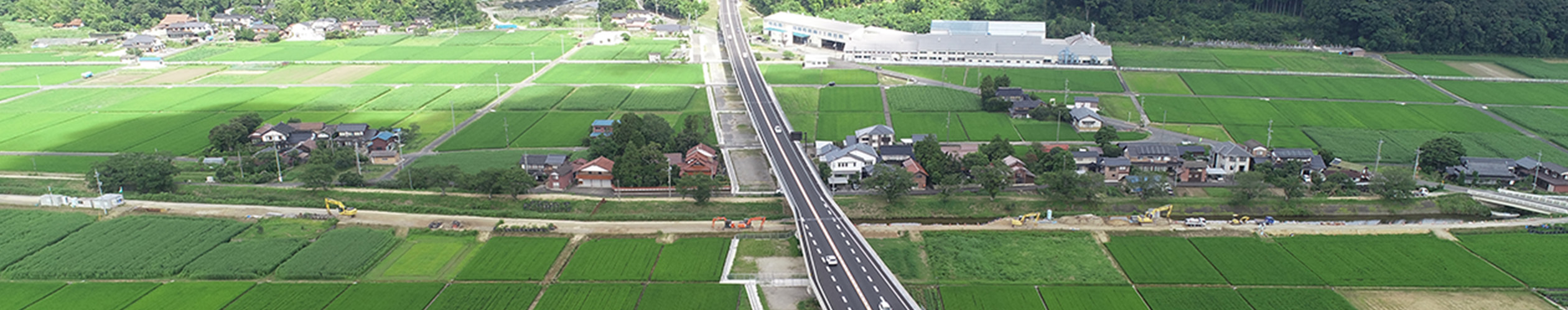 緑豊かな田園風景が広がり、中央には大きな道路が通っている航空写真